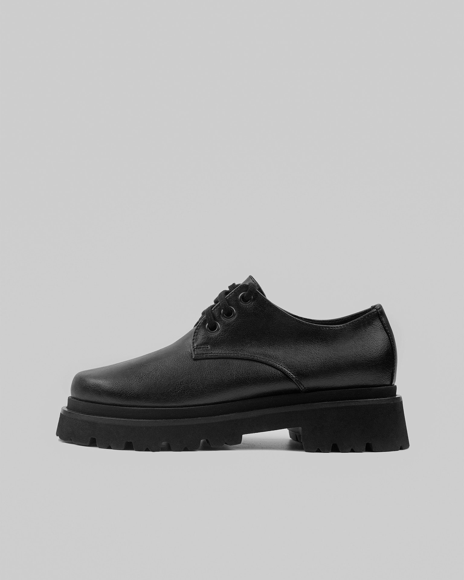 Black vegan leather lace-up shoe with chunky sole on a neutral background