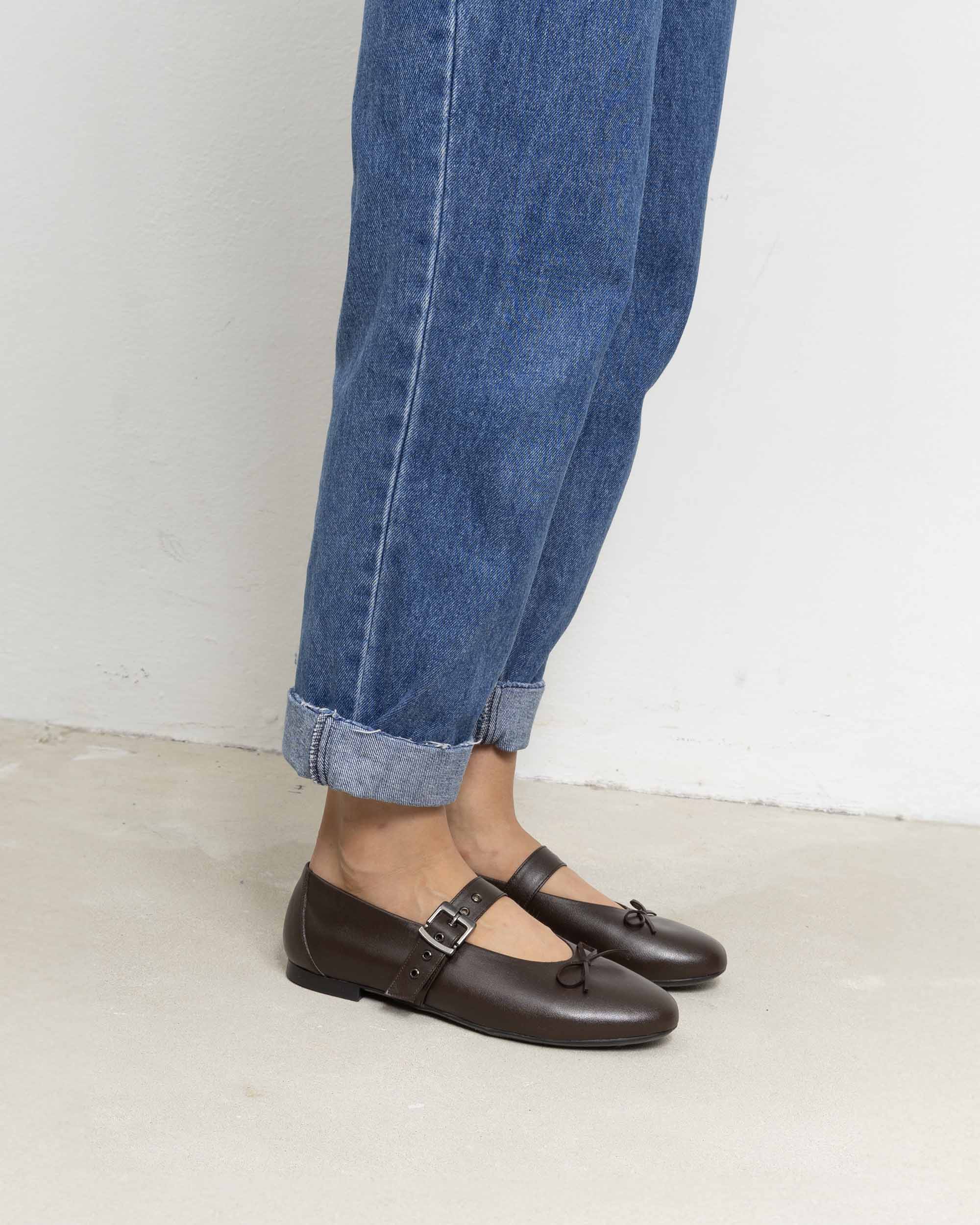 Woman wearing brown vegan Mary Jane shoes with buckle and bow, paired with rolled-up blue jeans, BOHEMA footwear