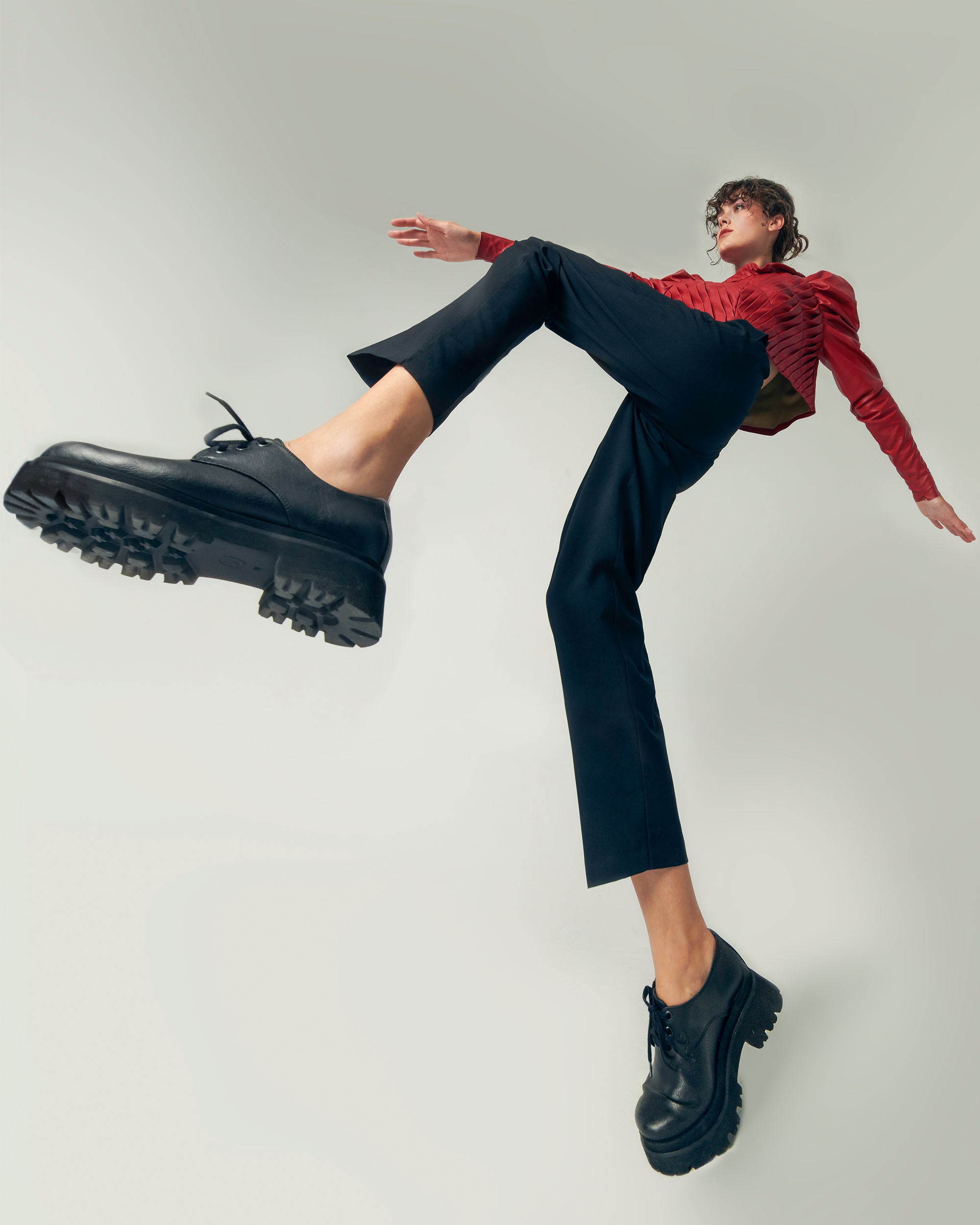 Person in red top and black pants posing mid-step wearing chunky black vegan shoes