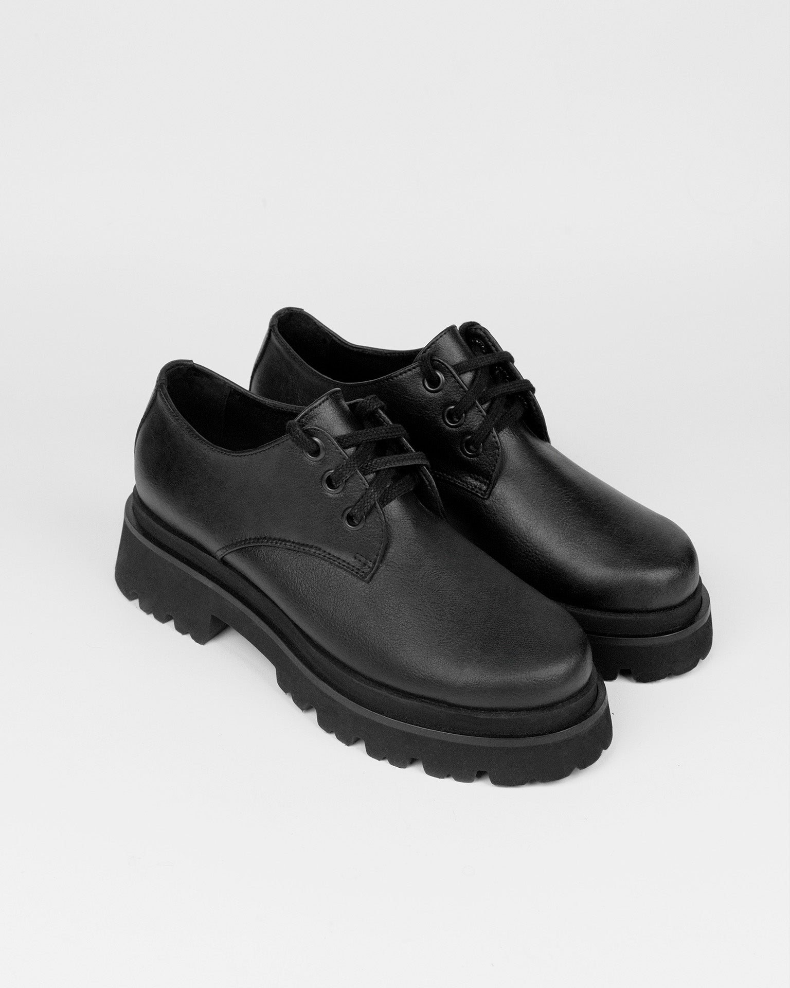 Black vegan leather lace-up shoes with chunky soles on white background