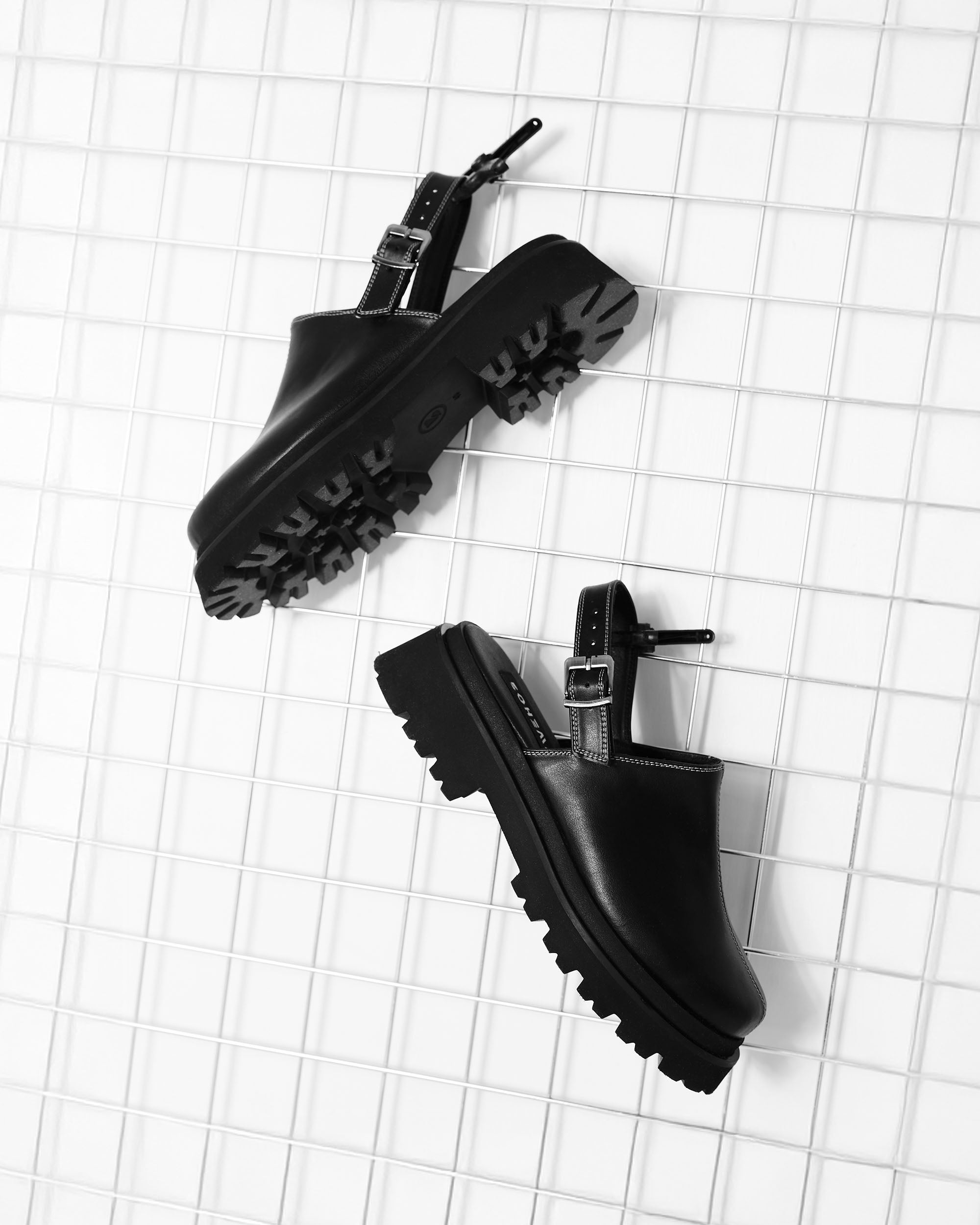 Black chunky sole slingback clogs with buckles on white grid background